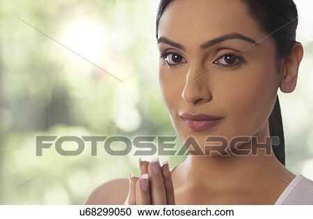 Stock Image - Close-up portrait of young woman with hands clasped against glass window. Fotosearch