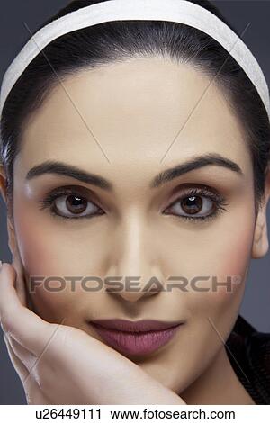 Stock Image - Close-up shot of a beautiful female with hand on her face over colored background . Fotosearch
