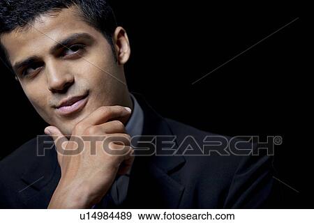 Stock Photo - Confident business man with hand on chin over black background . Fotosearch