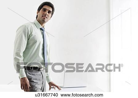 Confident businessman standing nearby laptop View Large Photo Image Stock Image - Confident businessman standing nearby laptop . Fotosearch