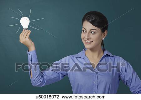 Confident young businesswoman holding light bulb against green board at office View Large Photo Image Stock Image - Confident young businesswoman holding light bulb against green board at office. Fotosearch