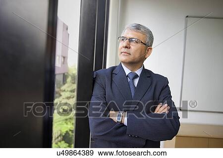 Stock Photo - Contemplative mature businessman looking through window at workplace . Fotosearch