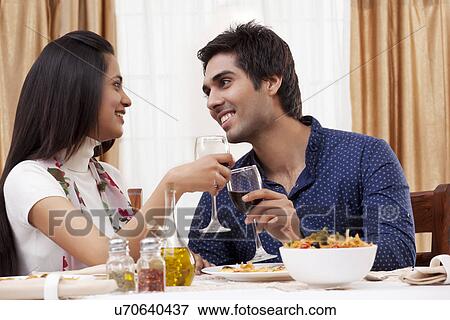 Stock Photo - Couple looking at each other while clinking wine glass at restaurant . Fotosearch