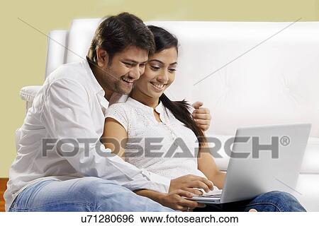 Couple sitting with a laptop View Large Photo Image Stock Photograph - Couple sitting with a laptop . Fotosearch