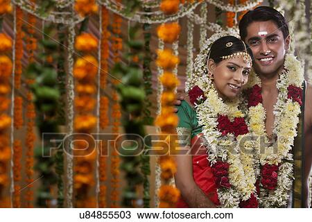 Stock Image - Couple wearing garlands standing together on their wedding day . Fotosearch