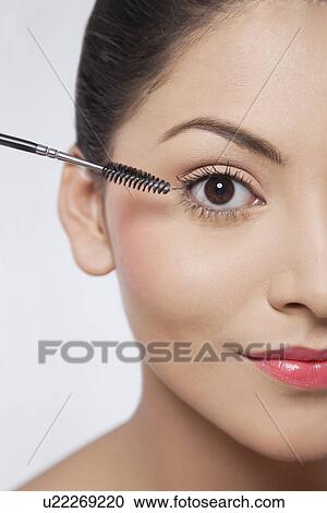 Stock Image - Cropped image of young beautiful woman applying mascara . Fotosearch