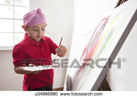Stock Image - Cute little boy standing in front of canvas with a paintbrush . Fotosearch