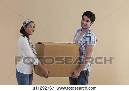 Stock Photo - Cute young couple holding cardboard box together while moving in . Fotosearch