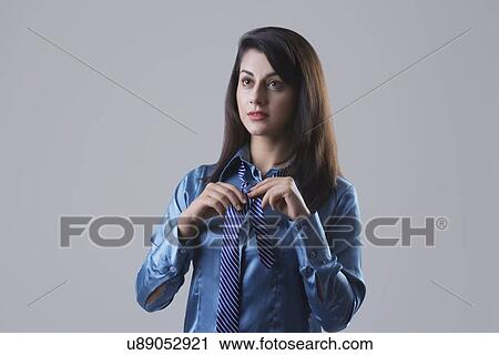 Determined businesswoman tying tie against gray background View Large Photo Image Stock Image - Determined businesswoman tying tie against gray background. Fotosearch