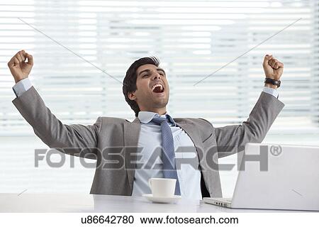 Excited young businessman at his desk celebrating success View Large Photo Image Stock Image - Excited young businessman at his desk celebrating success . Fotosearch