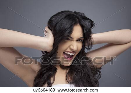 Stock Photo - Excited young woman with her hands covering her ears over colored background . Fotosearch