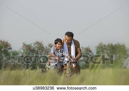 Stock Photograph - Father teaching son to ride cycle in the field . Fotosearch