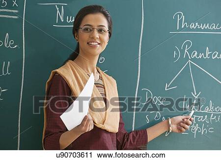 Female teacher explaining a lesson while standing against chalkboard View Large Photo Image Stock Image - Female teacher explaining a lesson while standing against chalkboard . Fotosearch
