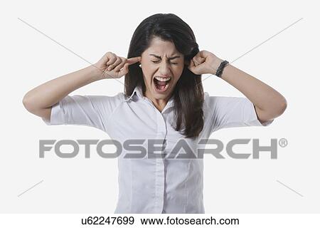 Stock Photo - Frustrated businesswoman with fingers in ears yelling against white background. Fotosearch