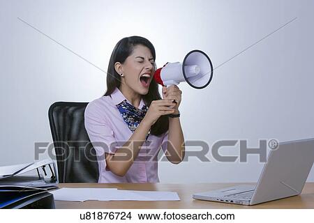 Frustrated businesswoman yelling in megaphone at office desk View Large Photo Image Picture - Frustrated businesswoman yelling in megaphone at office desk. Fotosearch