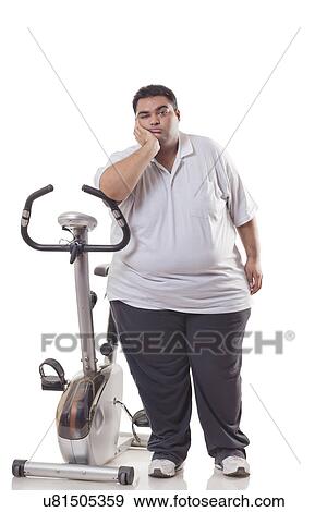 Full length of a tired obese man standing next to an exercise bike over white background  View Large Photo Image Stock Photo - Full length of a tired obese man standing next to an exercise bike over white background . Fotosearch