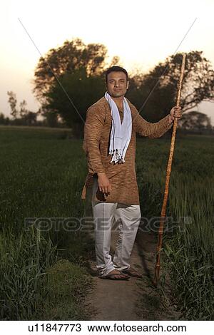 Stock Image - Full length of an Indian farmer standing with a stick . Fotosearch