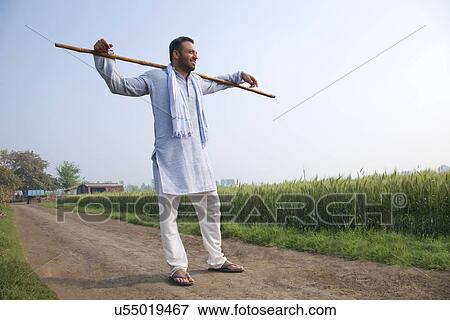 Stock Photo - Full length of an Indian man standing with a stick across his shoulders . Fotosearch