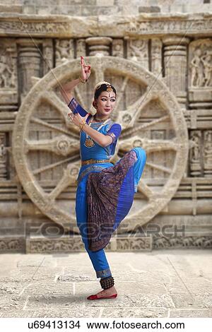 Picture - Full length of Bharatanatyam dancer performing against carved wall. Fotosearch