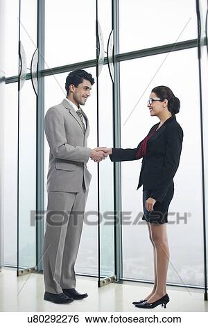 Stock Photograph - Full length of business people shaking hands in office. Fotosearch