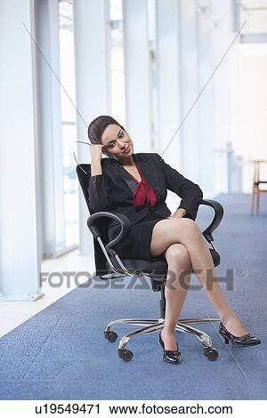 Stock Image - Full length of businesswoman relaxing on chair in office. Fotosearch