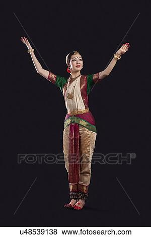 Full length of dancer with arms raised performing Bharatanatyam against black background View Large Photo Image Stock Photo - Full length of dancer with arms raised performing Bharatanatyam against black background. Fotosearch