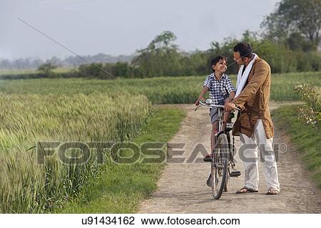 Full length of father assisting son to ride cycle View Large Photo Image Stock Image - Full length of father assisting son to ride cycle . Fotosearch