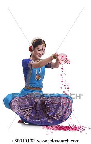 Stock Image - Full length of female Bharatanatyam dancer dropping rose petals over white background. Fotosearch