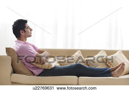 Full length of handsome young man day dreaming on sofa View Large Photo Image Stock Image - Full length of handsome young man day dreaming on sofa . Fotosearch