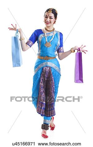 Stock Image - Full length of happy Bharatanatyam dancer with shopping bags posing over white background. Fotosearch