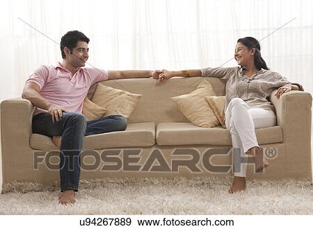 Full length of smiling young couple holding hands on sofa View Large Photo Image Stock Photo - Full length of smiling young couple holding hands on sofa . Fotosearch