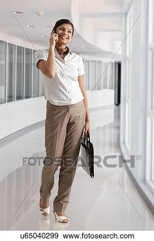 Full length of young businesswoman speaking on phone call with View Large Photo Image Stock Photo - Full length of young businesswoman speaking on phone call with . Fotosearch