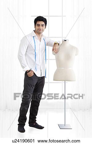 Stock Image - Full length of young male fashion designer standing by mannequin . Fotosearch