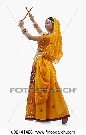 Stock Photo - Full length of young woman in chaniya choli performing Dandiya Raas over white background. Fotosearch