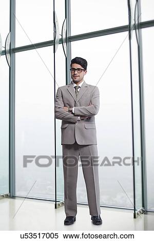 Stock Photography - Full length portrait of businessman standing arms crossed in office. Fotosearch