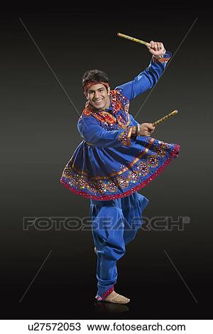 Stock Image - Full length portrait of man in traditional wear performing Dandiya Raas against black background. Fotosearch