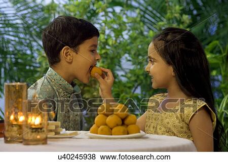 Girl feeding her brother a laddoo View Large Photo Image Stock Photo - Girl feeding her brother a laddoo . Fotosearch