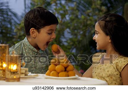 Stock Photograph - Girl feeding her brother a laddoo . Fotosearch