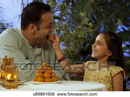 Girl feeding her father a laddoo View Large Photo Image Stock Photo - Girl feeding her father a laddoo . Fotosearch