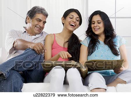 Girl looking at the family album with her parents View Large Photo Image Stock Photo - Girl looking at the family album with her parents . Fotosearch
