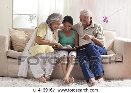 Stock Photo - Granddaughter looking at a photo album with her grandparents. Fotosearch