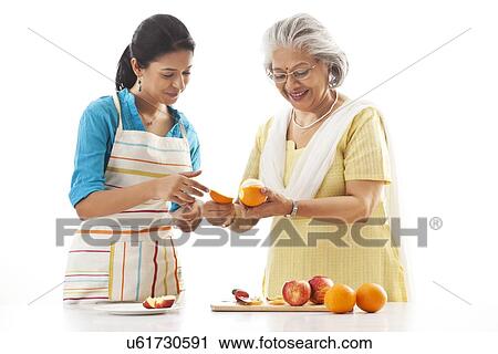 Stock Image - Grandmother and granddaughter cutting fruits. Fotosearch