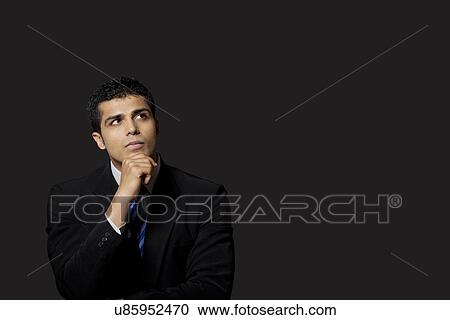 Stock Image - Handsome businessman looking away over black background . Fotosearch