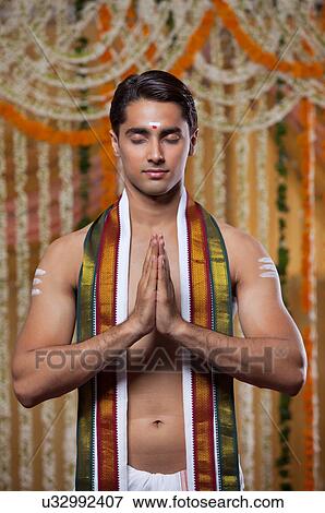 Handsome groom praying with garlands hanging in background View Large Photo Image Stock Photo - Handsome groom praying with garlands hanging in background . Fotosearch