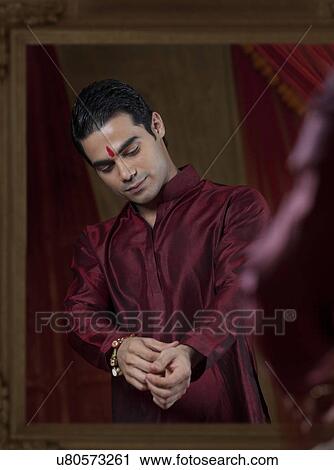 Stock Image - Handsome young bridegroom's reflection in mirror while getting dressed . Fotosearch