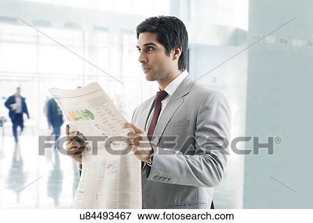 Handsome young business man looking away with newspaper in hand View Large Photo Image Stock Photo - Handsome young business man looking away with newspaper in hand . Fotosearch