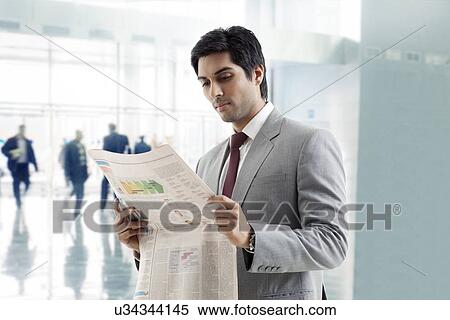 Handsome young businessman reading newspaper in office building View Large Photo Image Stock Photography - Handsome young businessman reading newspaper in office building . Fotosearch