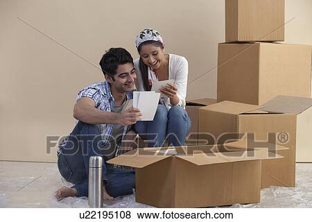 Stock Photo - Handsome young couple looking at photographs in their new home . Fotosearch