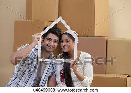 Handsome young couple smiling while looking through house shaped frame View Large Photo Image Stock Photo - Handsome young couple smiling while looking through house shaped frame . Fotosearch