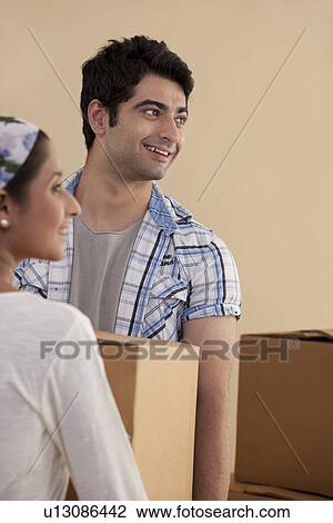 Stock Image - Handsome young man carrying cardboard box with woman while moving in . Fotosearch
